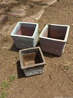 Three square ceramic planters arranged on soil showing size comparison and embossed design