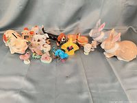 Group shot of all porcelain/ceramic figurines including pig bank, rabbits, dog, basket, bowls and miniatures