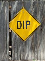 Yellow diamond DIP sign leaning against wooden fence