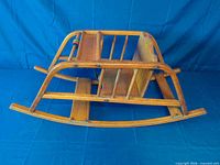 Underside view of wooden child rocking chair showing rocker runners, slatted construction and bead toy