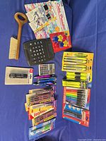 All items laid out showing calculators, brush, photo albums, packaged pens, markers, highlighters, loose pens