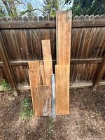 Front view of assorted boards, plywood sheet and wire mesh roll leaning against fence