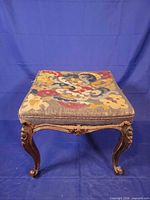 Full view of ottoman showing carved legs and needlepoint top