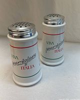 two white ceramic shakers with metal lids and Italian text