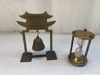 Pagoda-style brass gong bell and brass hourglass timer side by side