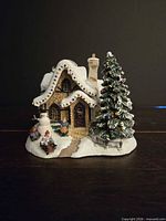 Front view of illuminated cottage showing decorated tree, roof bulbs, snowman and figures