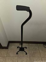 Full view of black aluminum quad cane showing foam handle, offset shaft and four-point base