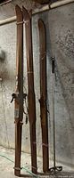 Three pairs of wooden skis and single bamboo pole leaning against wall