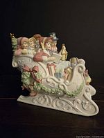 Left side of porcelain sleigh showing carolers and decorative garland