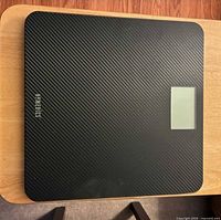 Top view of black HoMedics scale showing carbon-fiber texture and LCD area