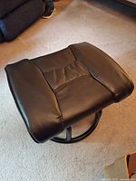Overall view of black leather gliding footrest showing top upholstery and circular base
