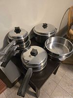 Group view of cookware, showing handles, lids, and nested pans on table