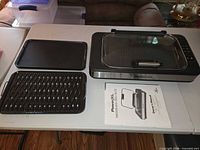 Overall view of grill base, two loose cooking trays, and manual
