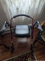 Front view of maroon rollator walker showing seat, backrest and hand brakes