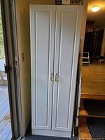 Front view of tall white cabinet with double doors and handles