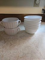 Stack of two handled soup cups beside stack of six small bowls