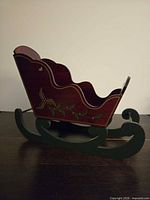 Left side view of red wooden sleigh with holly design and green runners