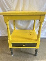 Front view of yellow side table showing drawer, turned legs and shelf