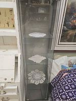 Front view showing entire glass curio cabinet with three glass shelves and black base/top
