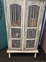 Front view of distressed white and gray louvered cabinet on legs