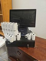 Front view of touchscreen terminal, cash drawer, printer and stacked paper rolls