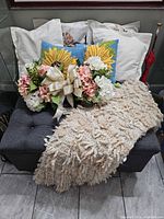 All items grouped on ottoman: throw, two sunflower pillows, floral arrangement, seasonal covers partly visible