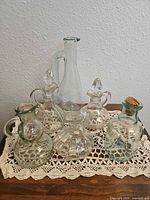 Group shot of six assorted glass decanters on lace mat