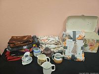 Group shot of dress package, stacked scarves, ceramic teapot, sugar bowl, creamers and storage box