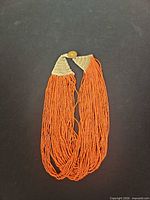 Full view of multi-strand orange bead necklace with crocheted ends and metal button toggle
