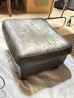 Top view of black leather ottoman showing surface creasing and scuffs