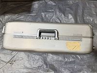 Top view of closed silver aluminum suitcase showing carry handle, combination lock, and adhesive residue