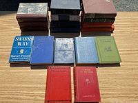 All 19 books arranged on table; shows mixture of cloth colors and stacked spines