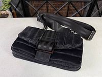 Full view of bag showing quilted exterior, buckle detail, zipper perimeter and adjustable strap