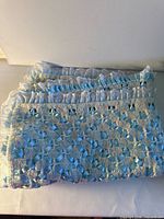 Folded light blue crochet baby blanket showing ribbon weave and lace edge