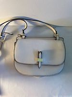 Front view of white faux leather crossbody bag showing gold accent, black piping and adjustable strap