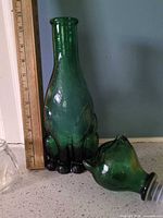 Green glass cat decanter body beside ruler for height reference; small clear glass piece visible