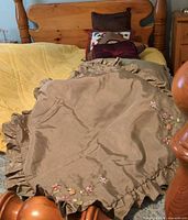 Bed showing taupe ruffled embroidered shams and stack of assorted pillows at headboard