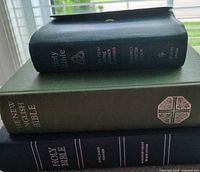 Stack of three Bibles showing spines, sizes, cover colors, wrap flap visible