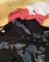 All three garments laid out: black floral cardigan, coral cardigan, white pullover