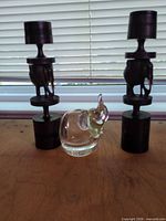Front view of two wooden elephant candlesticks and clear glass elephant paperweight