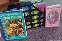 Front covers of The Field Guide to Wild Flowers, five unidentified books in mesh holder, and Tottering in My Garden