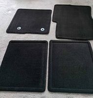 Four black carpet floor mats laid out, showing overall shape and condition