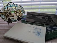 Group shot showing all four items: stained glass plaque, soapstone carving, book, tea towel