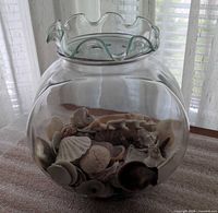 Top view of clear glass fishbowl vase filled with seashells, ruffled rim tray resting on opening