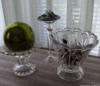 Overall view: two clear glass bowls, tall glass pedestal with pewter dolphin on top, green ornament ball, feathers