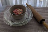 Stacked Pyrex plates, Corelle bowl with lid and candy tin inside, wooden rolling pin beside