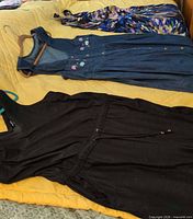 All three garments laid out: black jumpsuit, denim dress, patterned dress