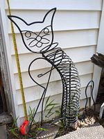 Full view of cat sculpture leaning against siding with tape measure for scale
