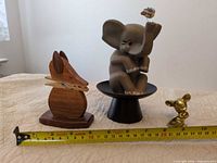 Group view of wooden fox, rubber elephant on pedestal, brass mouse with tape measure for scale