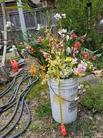 Full view of artificial flower arrangement standing in white plastic bucket outdoors